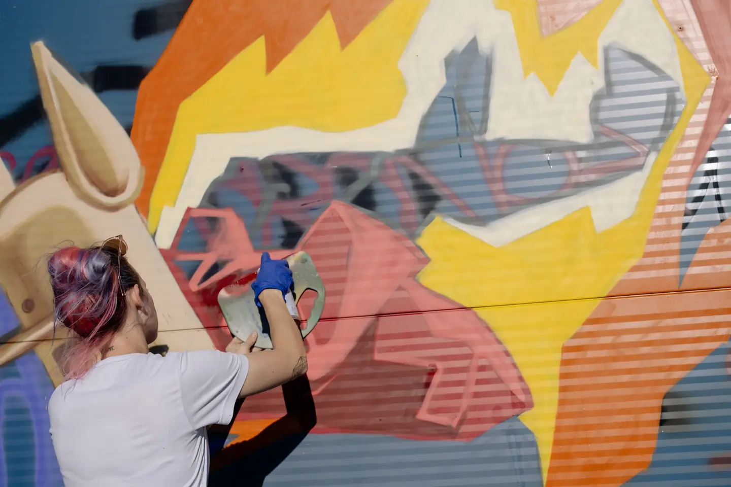 Artista pintando un mural de formas naranjas y amarillas sobre una pared
